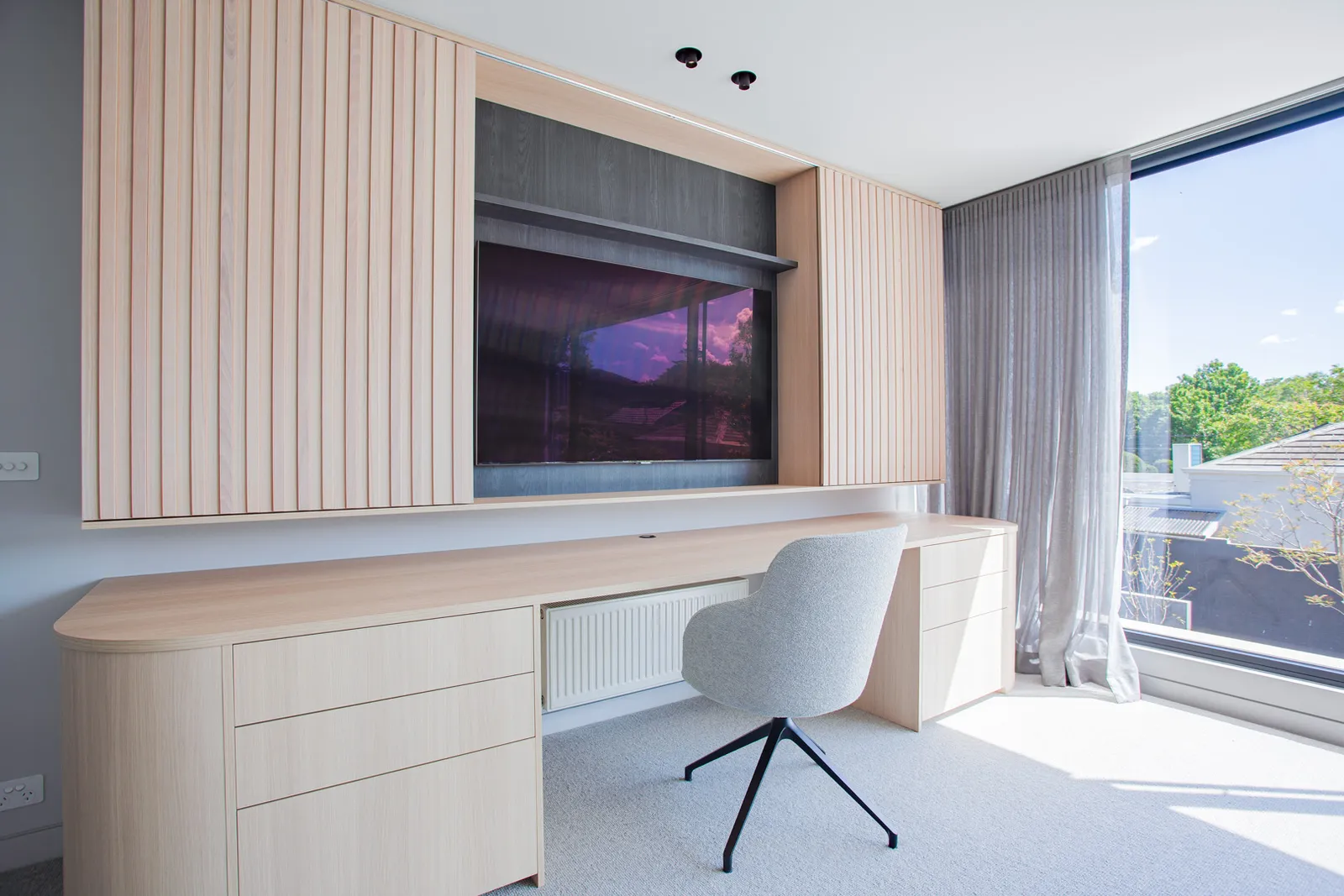 Timber built-in desk and wall unit with concealed TV, slat panelling and large glazed window