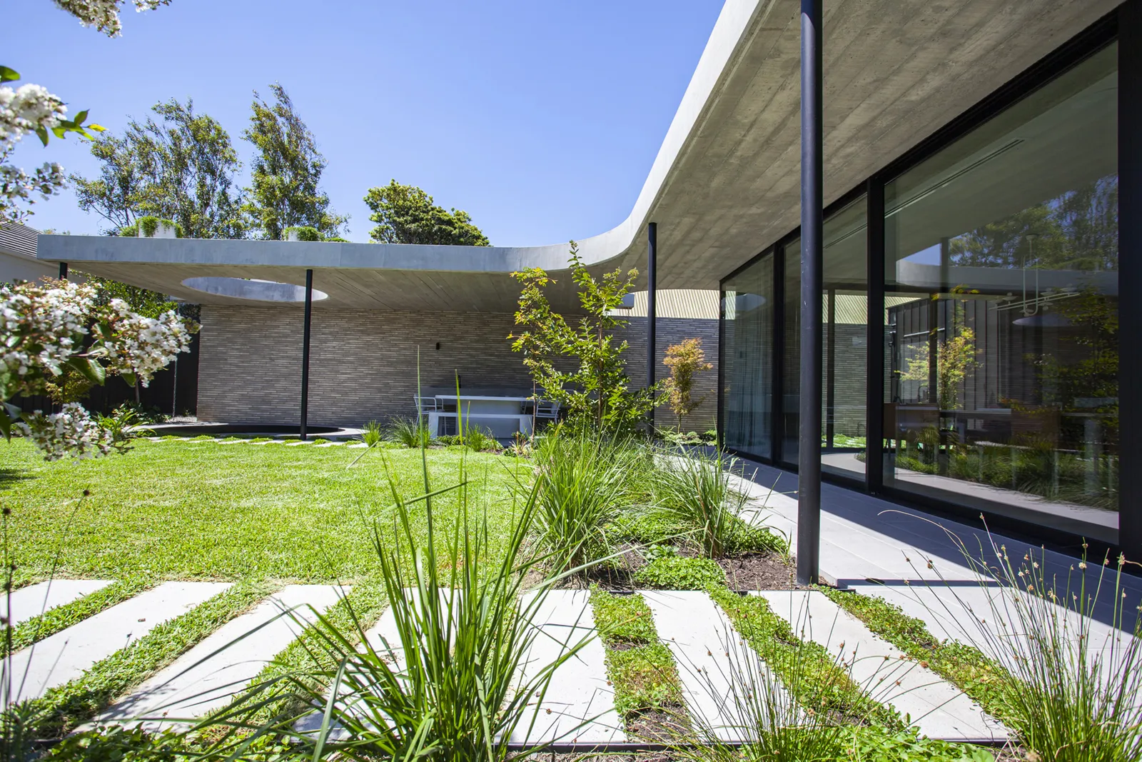 Courtyard garden with concrete canopy roof, glass walls, stone pavers and lush plantings