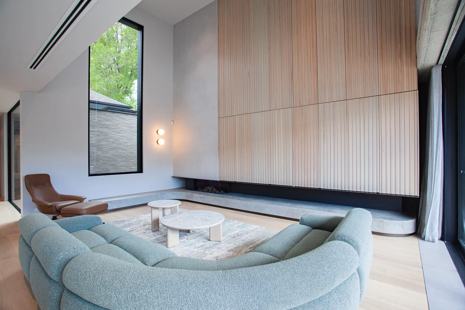 Bright living room with curved teal sofa, timber feature wall, and tall narrow window