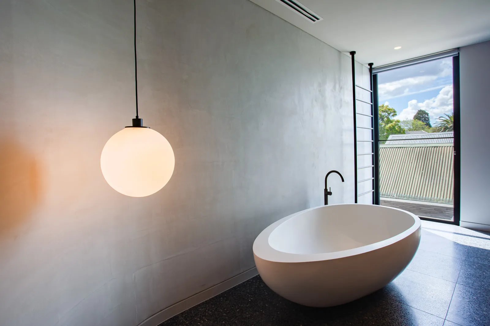 Freestanding oval bathtub with globe pendant light and large window overlooking greenery