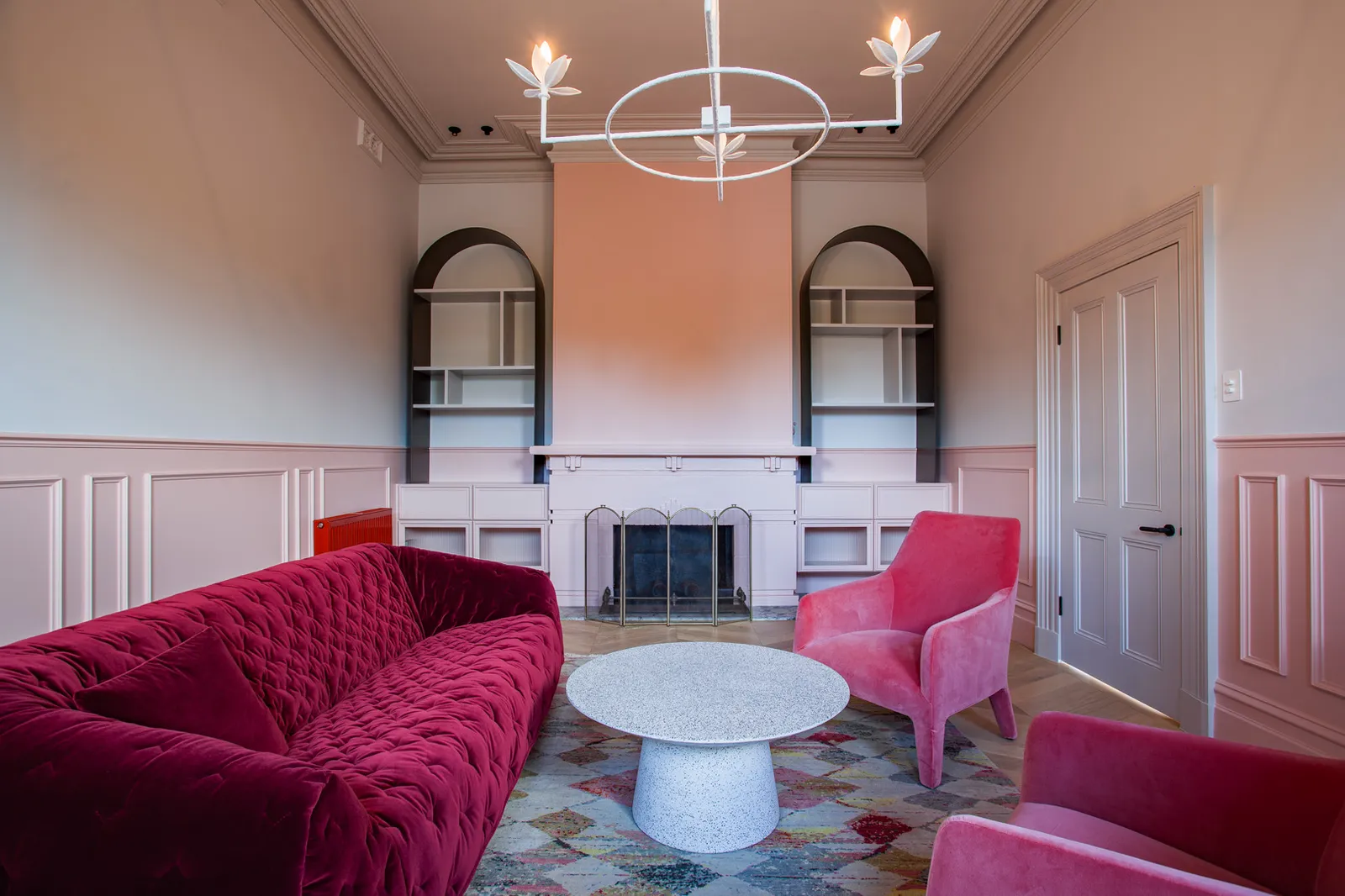 Formal sitting room with deep red velvet sofa, arched built-in shelving and ornate fireplace