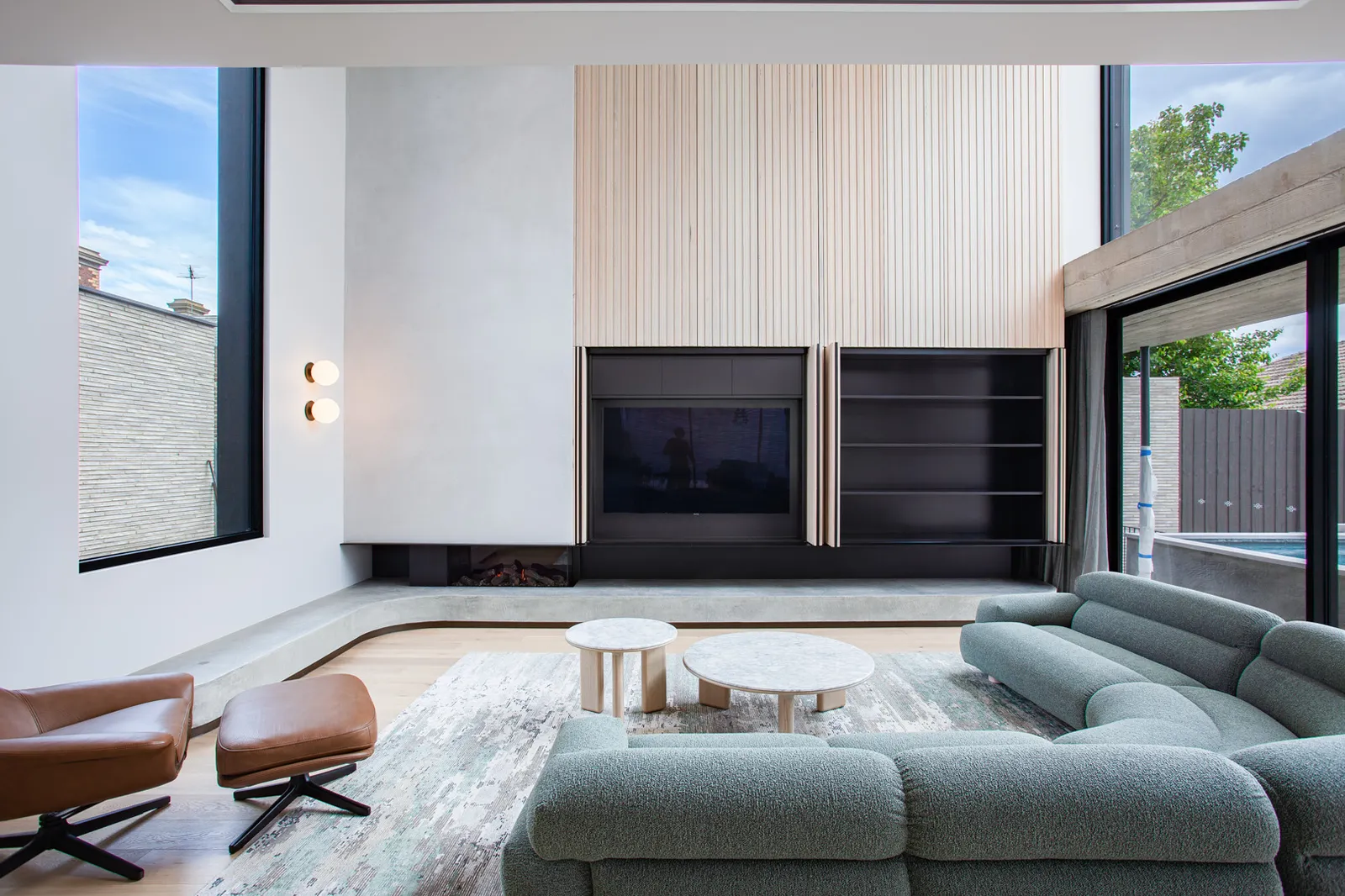 Open-plan living room with timber slat feature wall, gas fireplace, sectional sofa and pool view