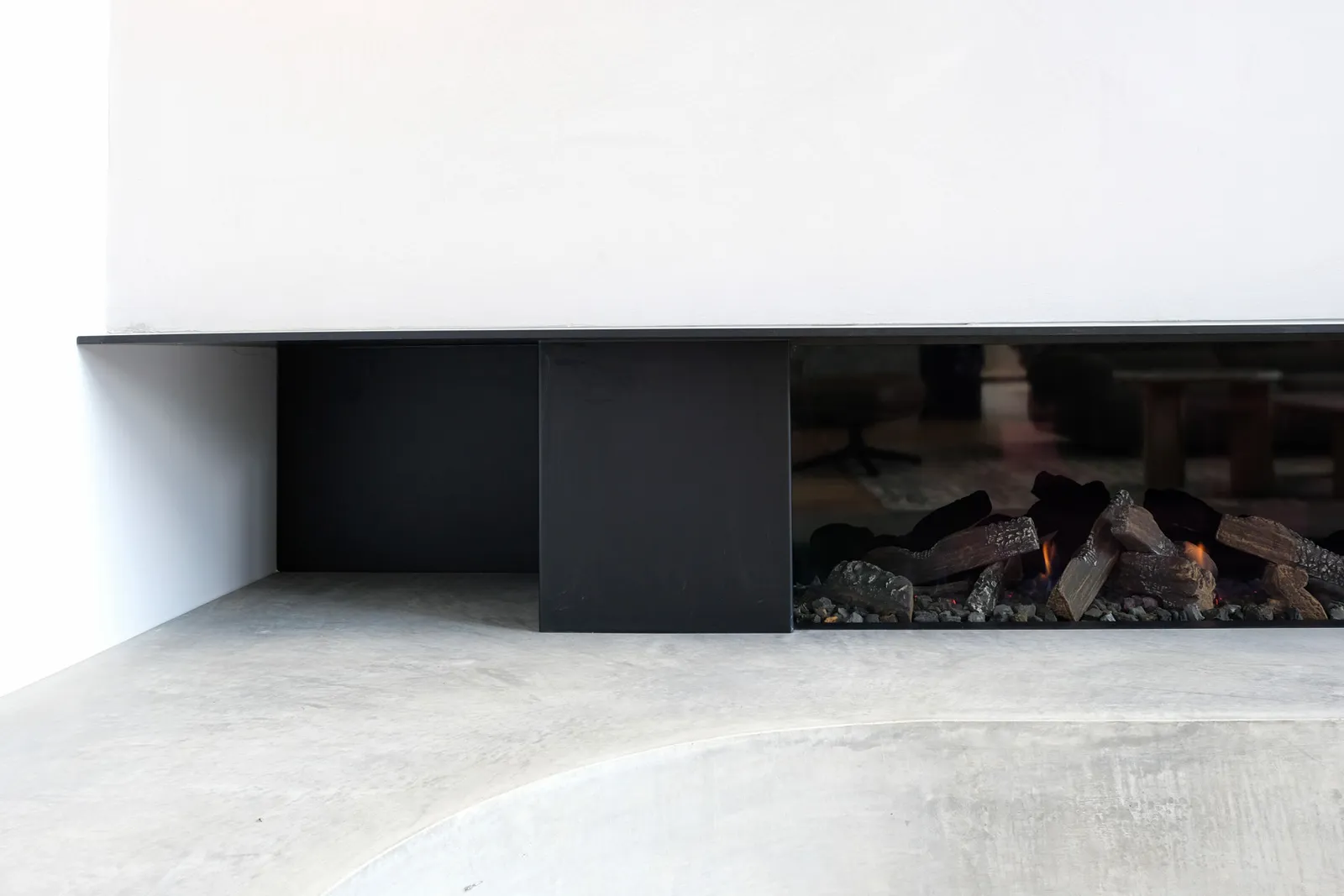 Close-up of recessed linear gas fireplace set in black steel surround on polished concrete floor