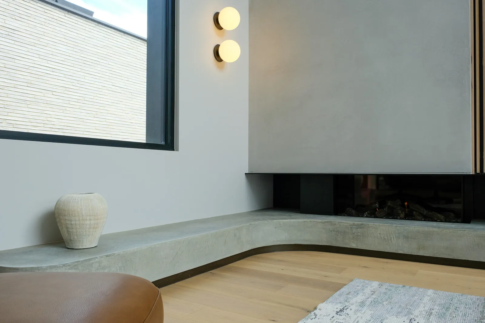 Curved concrete bench seat beside a linear gas fireplace with double globe wall sconces and timber floor