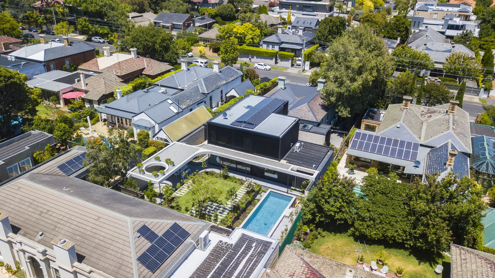 Aerial view of modern home with pool, courtyard and solar panels in suburban neighbourhood