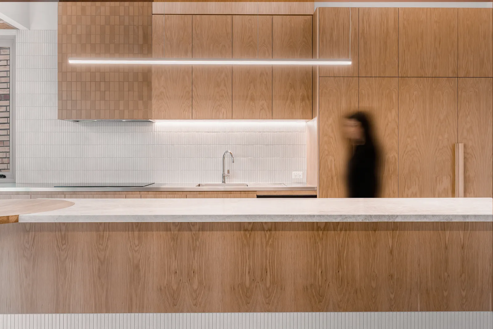 Oak kitchen cabinetry with under-cabinet LED lighting, white tile splashback and marble island