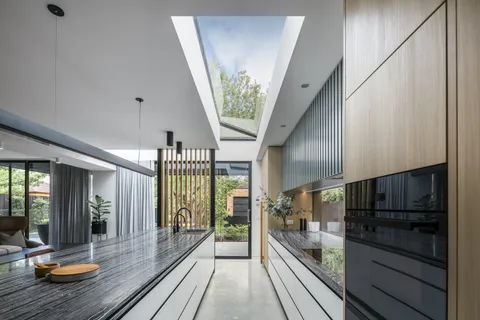 Open-plan kitchen with dark marble island, skylight, timber cabinetry, and garden views