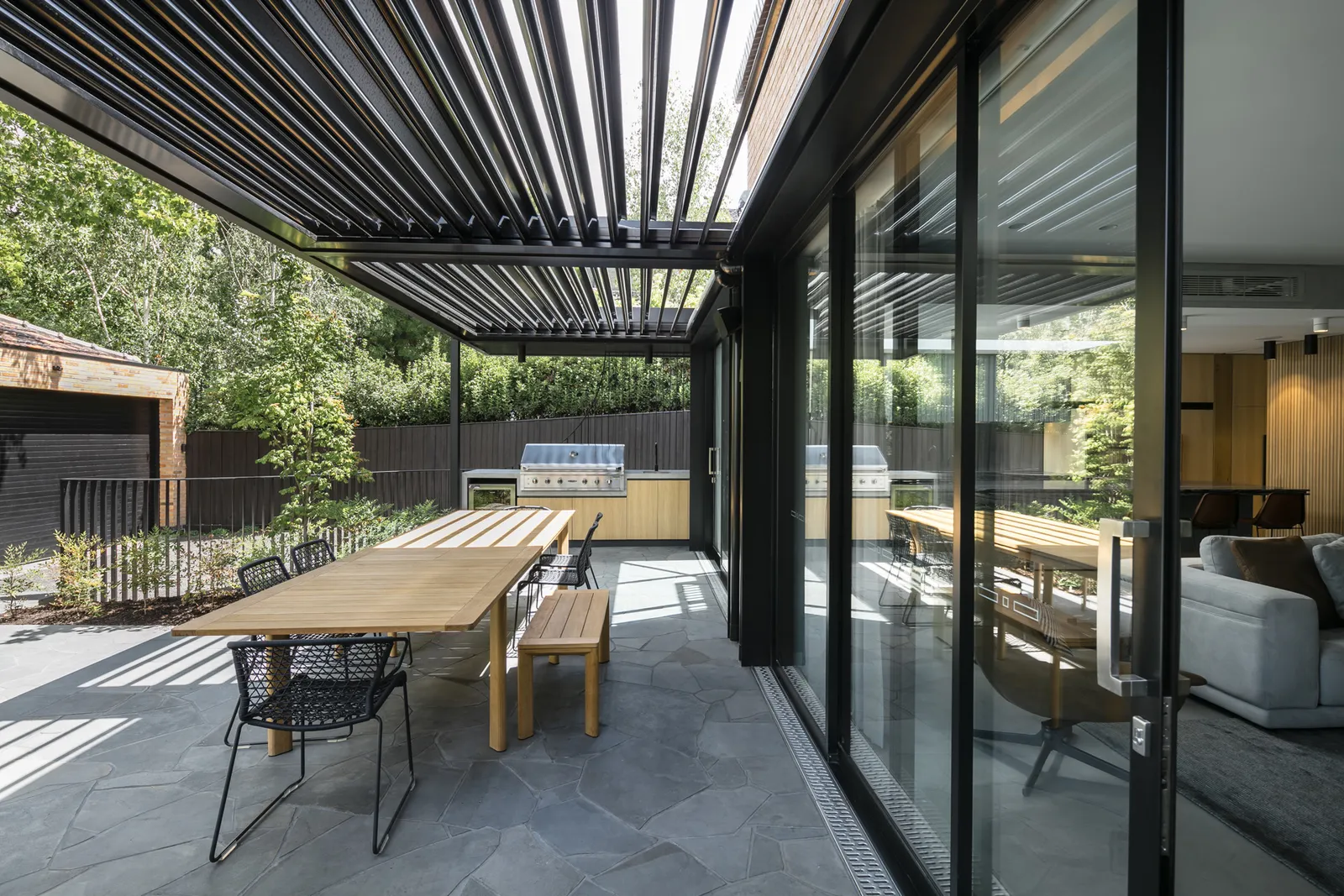 Covered outdoor alfresco with louvred pergola, timber dining table and BBQ kitchen