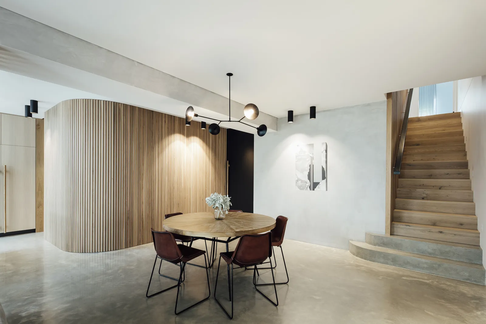 Dining room with round timber table, curved timber batten feature wall and timber staircase