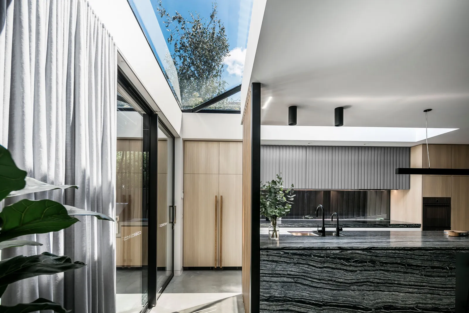 Open kitchen with black marble island, skylights, timber joinery and sheer curtains
