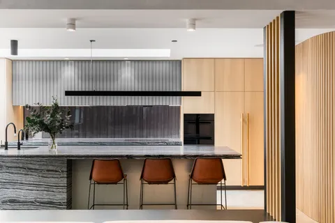 Modern kitchen island with marble benchtop, leather bar stools, and timber cabinetry wall