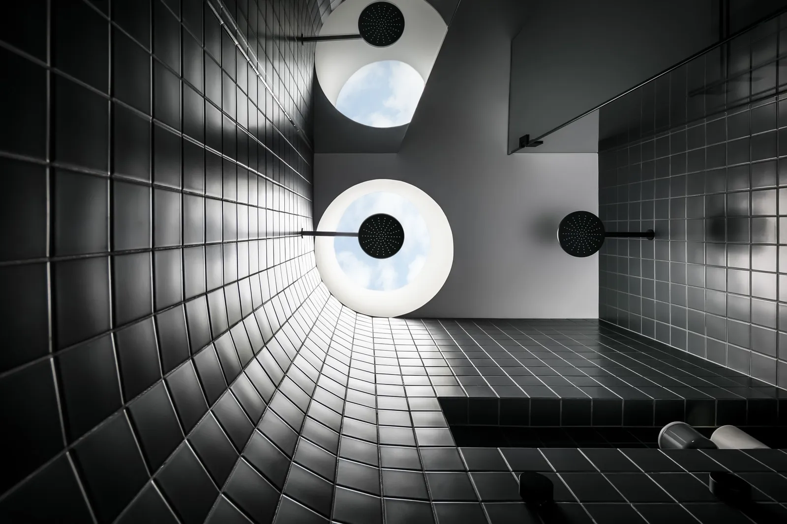 Dark tiled shower room viewed from below with round skylights and multiple overhead shower heads