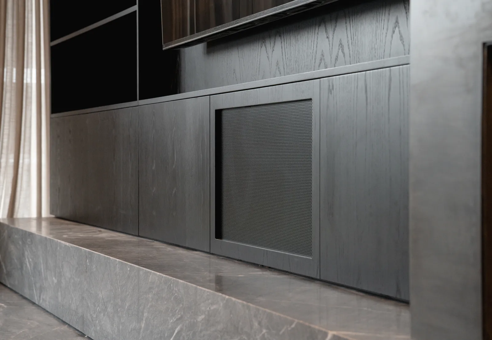 Close-up of dark timber joinery cabinetry with perforated metal grille panel and stone hearth