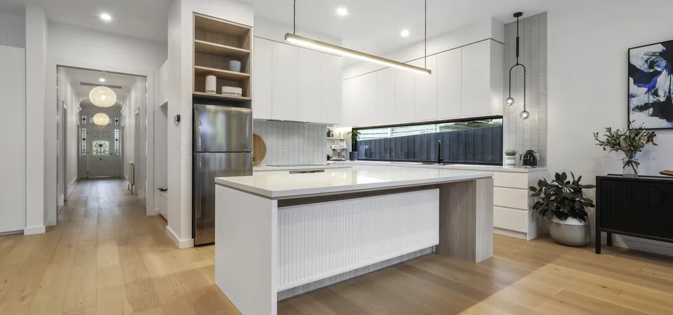 Modern white kitchen with island bench, timber floors, and hallway view