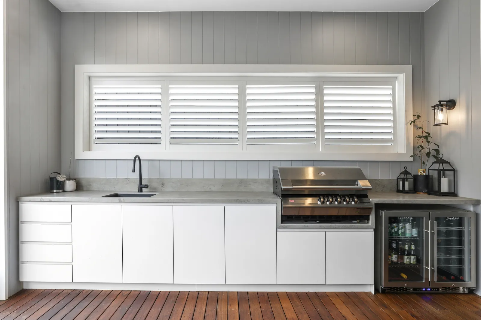 Outdoor alfresco kitchen with white cabinetry, BBQ, beverage fridge and plantation shutters