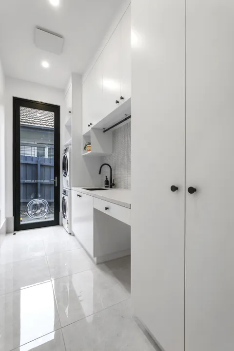 White laundry room with stacked washer-dryer, built-in cabinetry and black tapware
