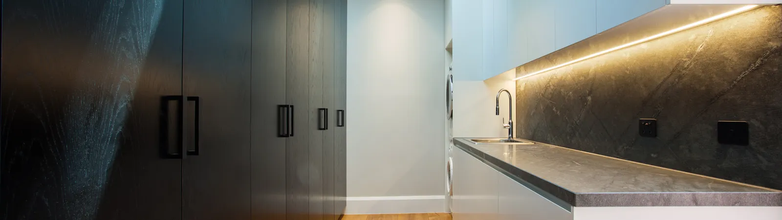 Sleek laundry or butler's pantry with dark joinery, stone benchtop, and skylight