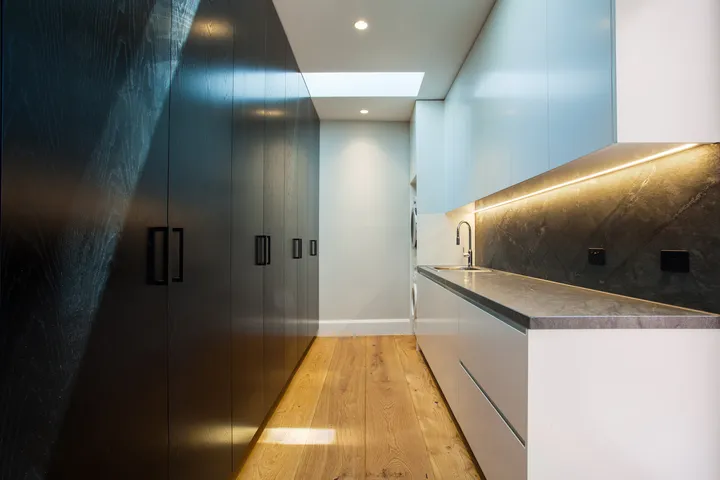 Sleek laundry or butler's pantry with dark joinery, stone benchtop, and skylight