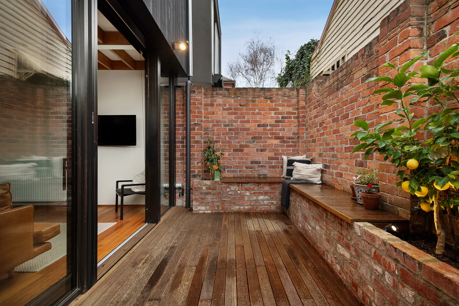 Timber deck courtyard with built-in brick bench seat, sliding glass doors opening to living room