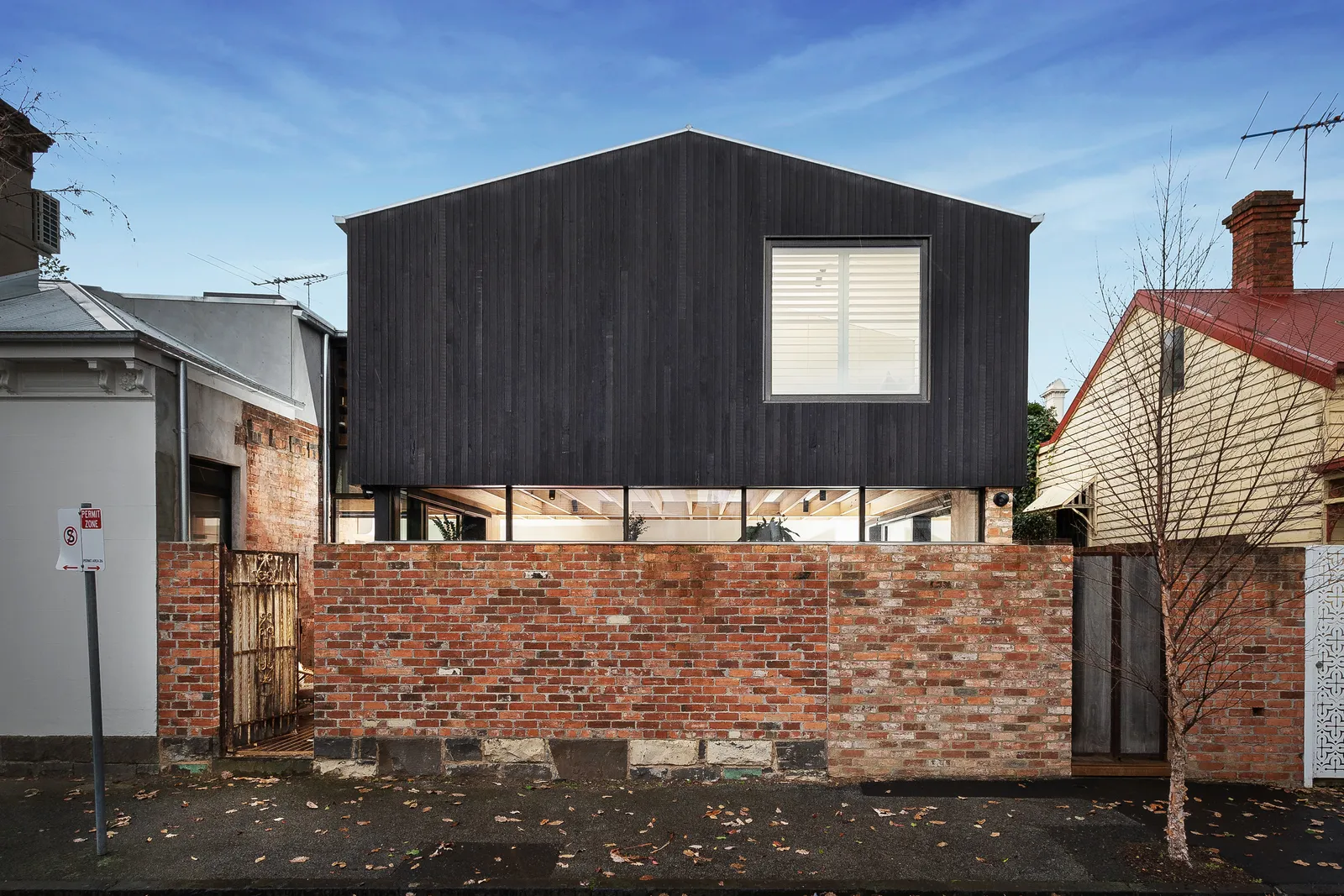 Street facade of dark charred timber upper storey above original exposed brick boundary wall