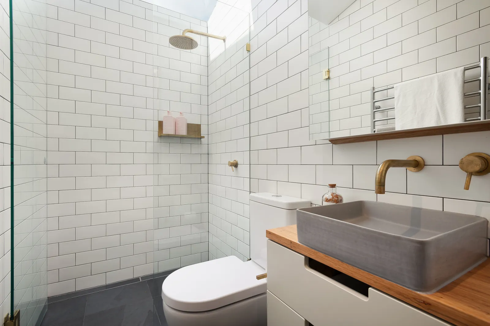 Bright bathroom with white subway tiles, concrete basin on timber vanity and brass fixtures