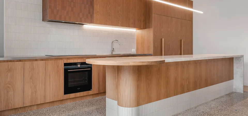 Open-plan timber kitchen with island bench, black oven, white tile splashback and terrazzo floor