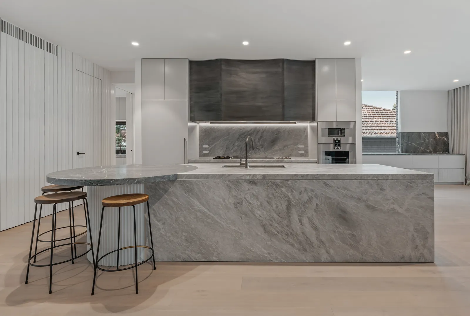 Modern kitchen with large marble island, bar stools, and integrated rangehood in renovated Kew home
