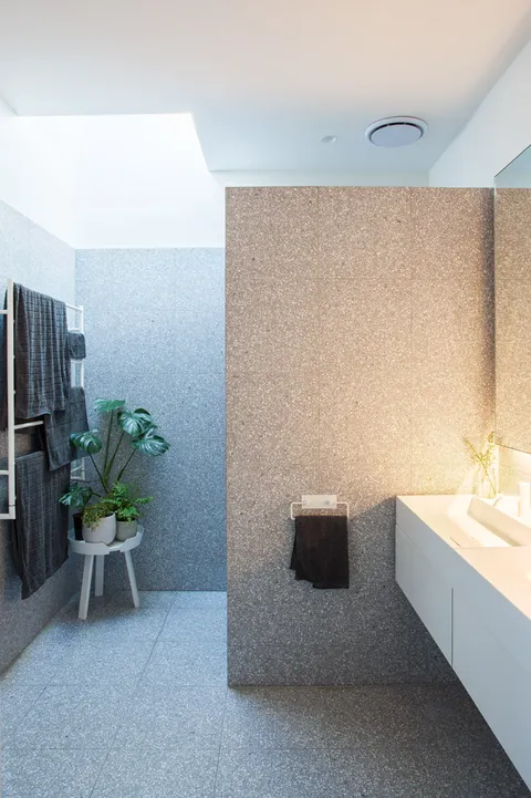 Modern bathroom with terrazzo walls, skylight, white vanity, towel ladder, and potted plants