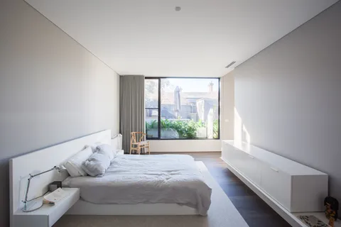Minimalist bedroom with low platform bed, floor-to-ceiling window, and floating bedside storage