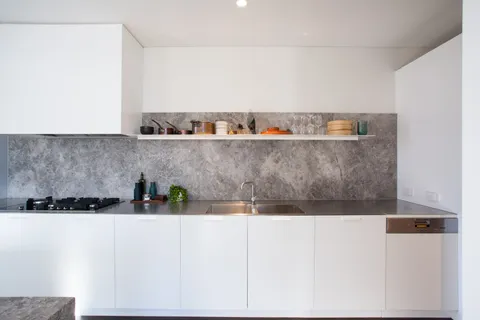 Modern kitchen bench with stone splashback, open shelf, stainless sink, and gas cooktop
