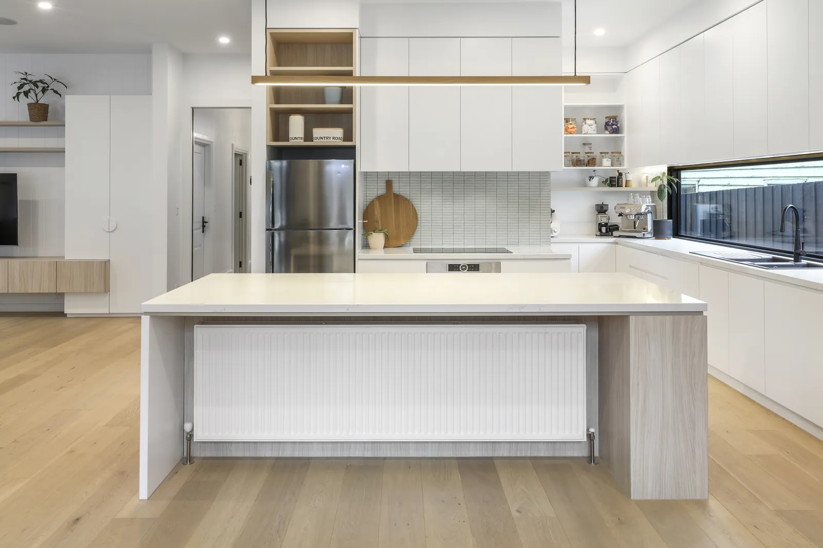 Bright kitchen with large island, white cabinetry, timber shelving and tiled splashback