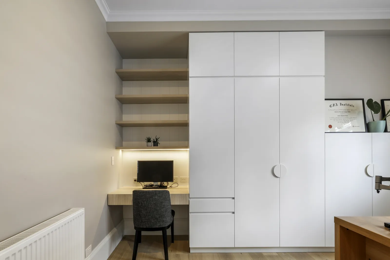Built-in study nook with floating timber shelves, desk, monitor and white wardrobe