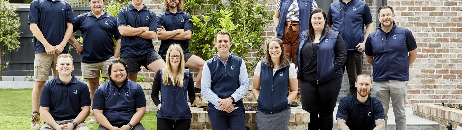 TCON team group portrait in navy uniforms posed in front of a brick wall outdoors