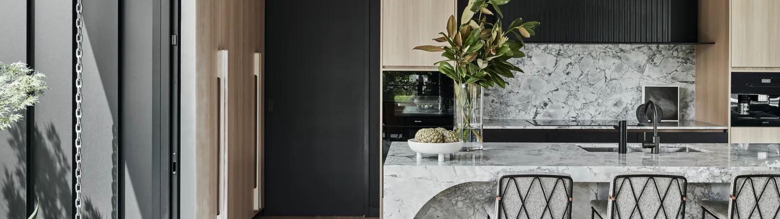 Modern kitchen with marble island, black cabinetry, timber floors and indoor plant