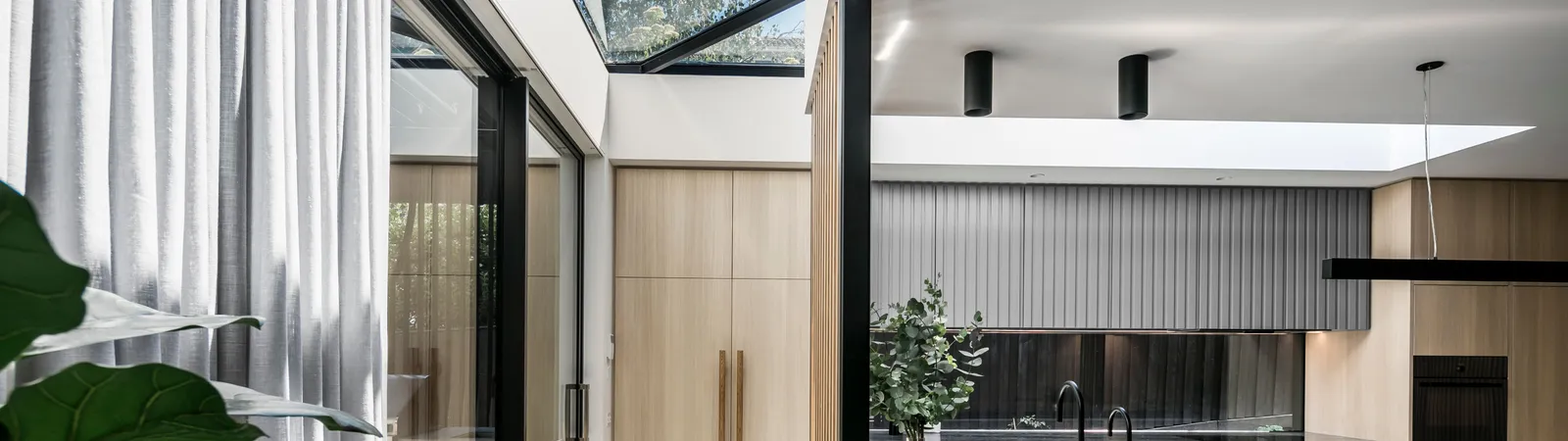 Modern open-plan kitchen with dark marble island, skylight, timber cabinetry and sheer curtains