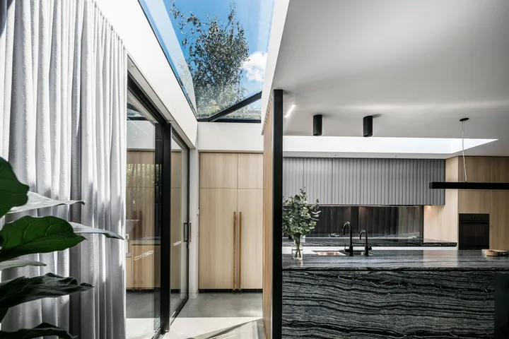 Modern open-plan kitchen with dark marble island, skylight, timber cabinetry and sheer curtains