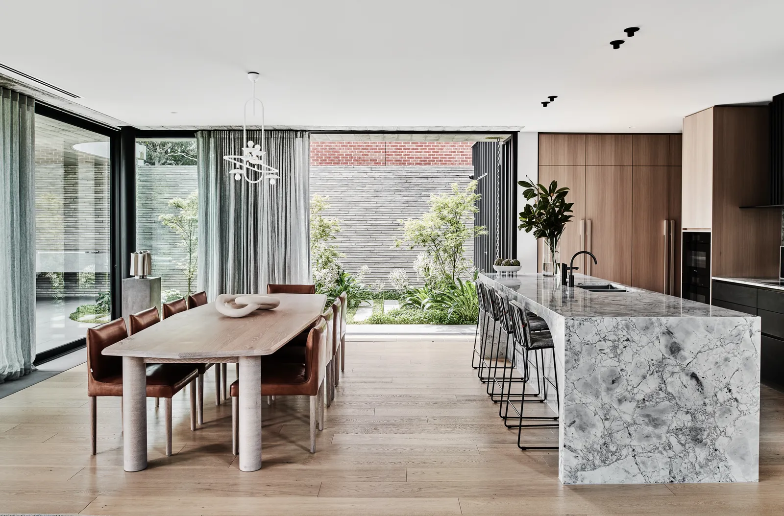 Open-plan kitchen and dining with marble island, timber cabinetry, leather chairs, and courtyard view