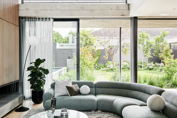 Curved grey sectional sofa with marble coffee table in bright living room overlooking lush garden