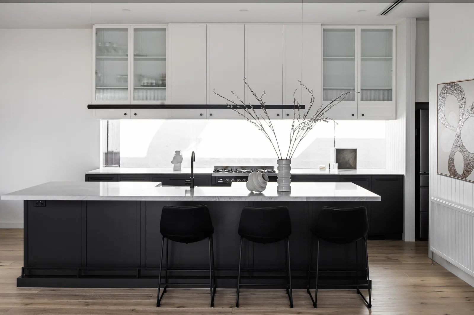 Monochrome kitchen with black island, white marble benchtop, glass upper cabinets and bar stools