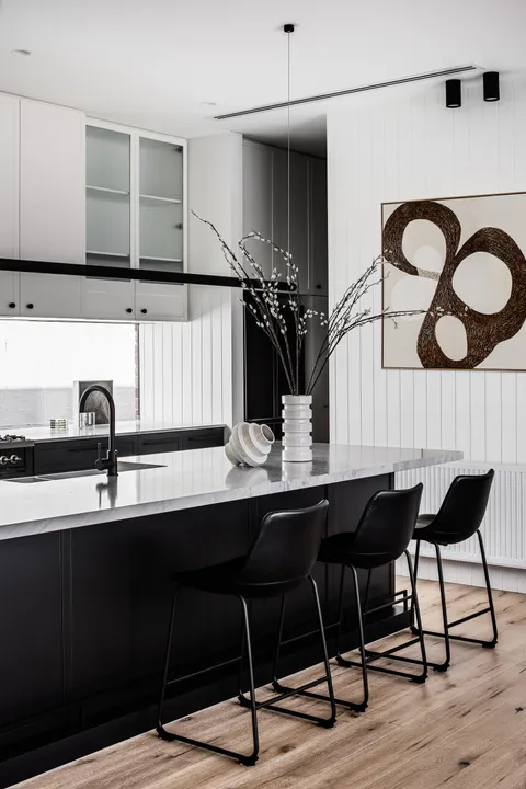 Monochrome kitchen with black island, marble benchtop, bar stools and abstract wall art