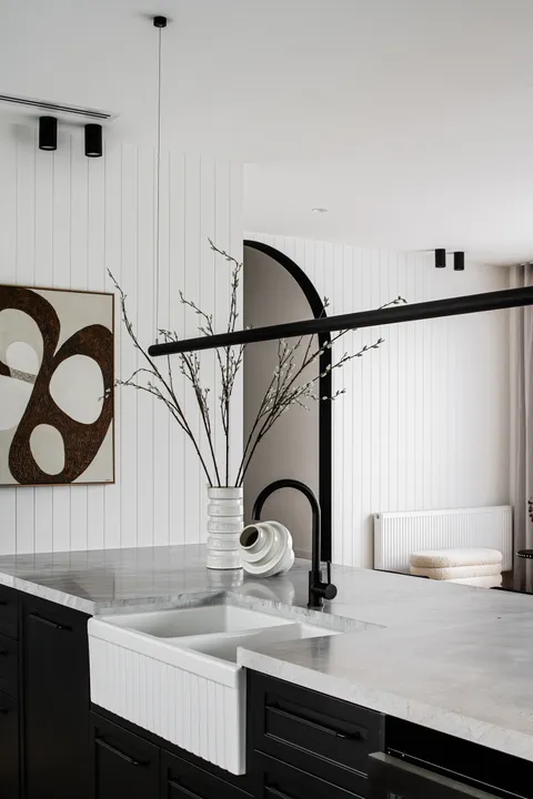 Close-up of marble kitchen sink with black tapware, pendant light and abstract artwork