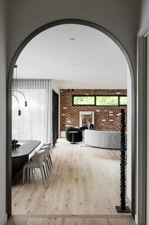 Arched doorway framing open-plan living and dining with exposed brick feature wall and timber floors