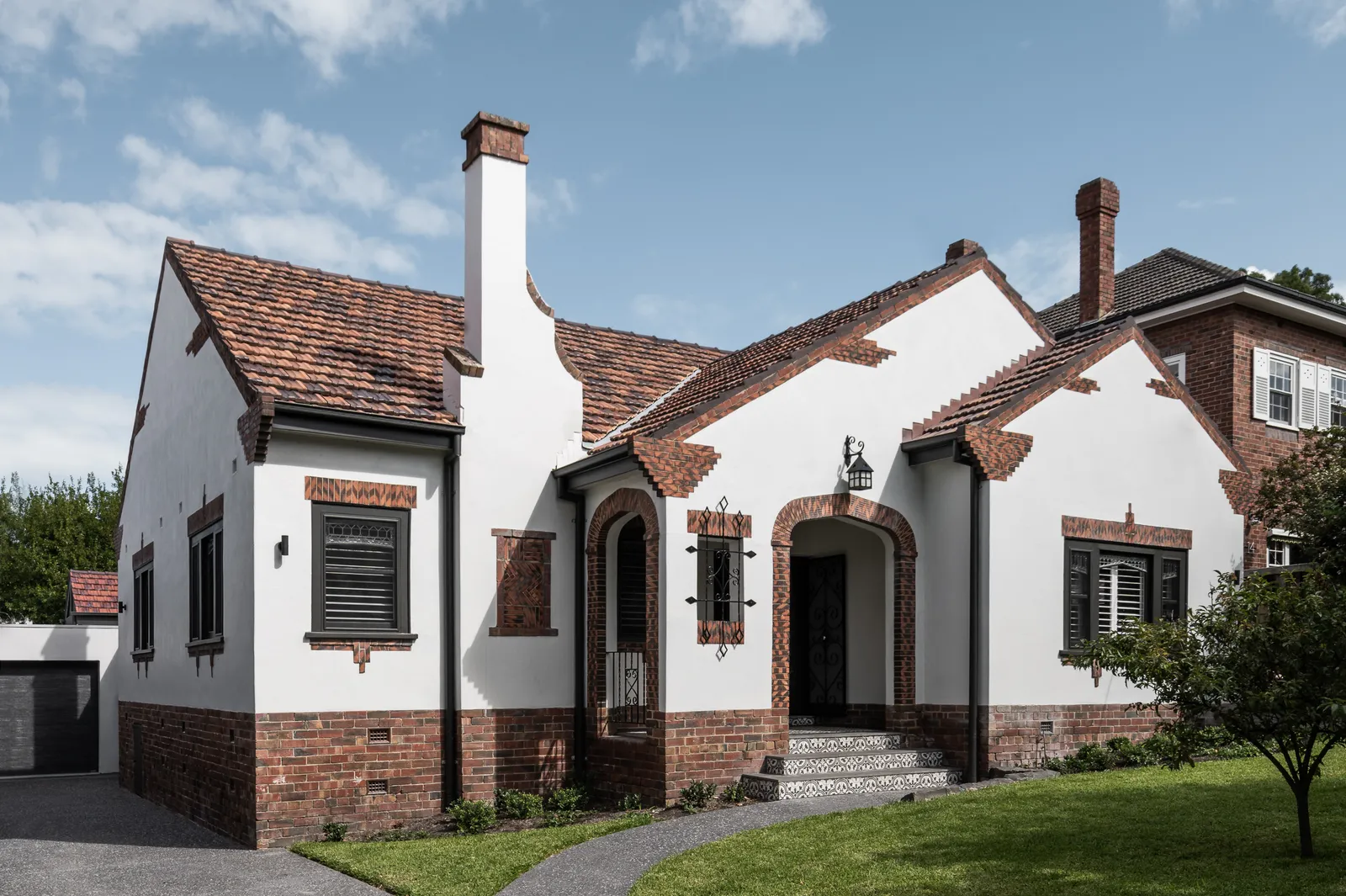 Full street-facing facade of art deco Camberwell home with tiled roof, brick detailing and arched entry