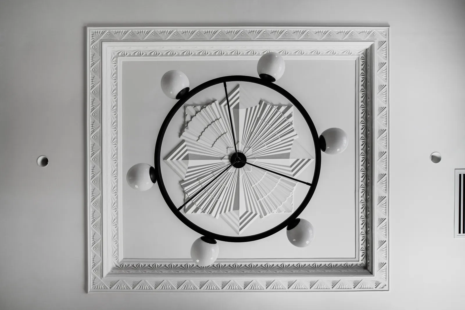 Overhead view of art deco plaster ceiling rose with geometric sunburst motif and circular chandelier