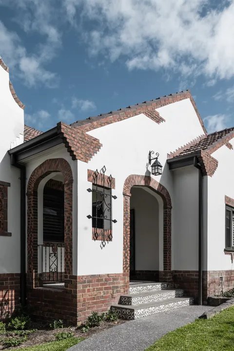 Art deco home entrance with brick arches, rendered facade, decorative ironwork and tiled steps