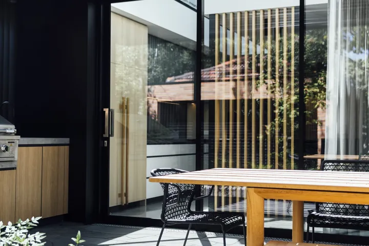 Covered outdoor dining area with timber table, black louvre pergola, and sliding glass doors