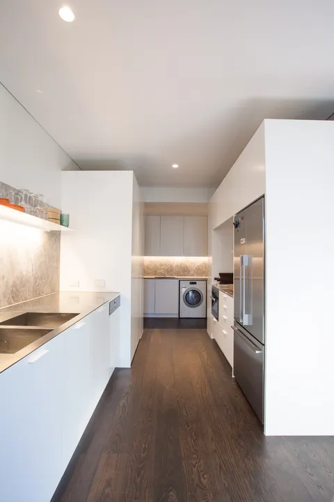 Narrow galley kitchen and laundry with white cabinetry, stone splashback, and timber floors