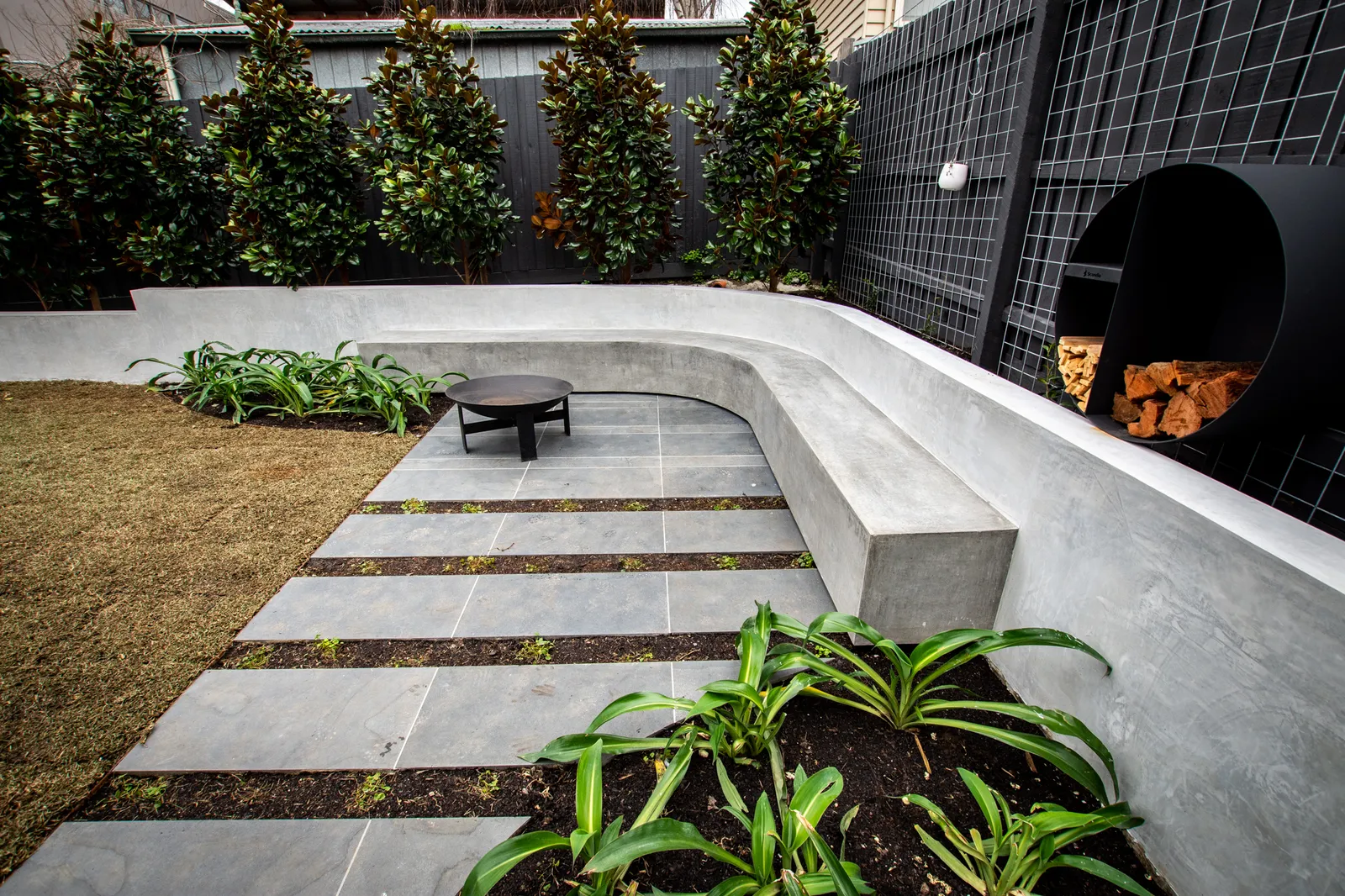 Landscaped backyard with concrete retaining wall, stone paving, fire bowl and espalier trees