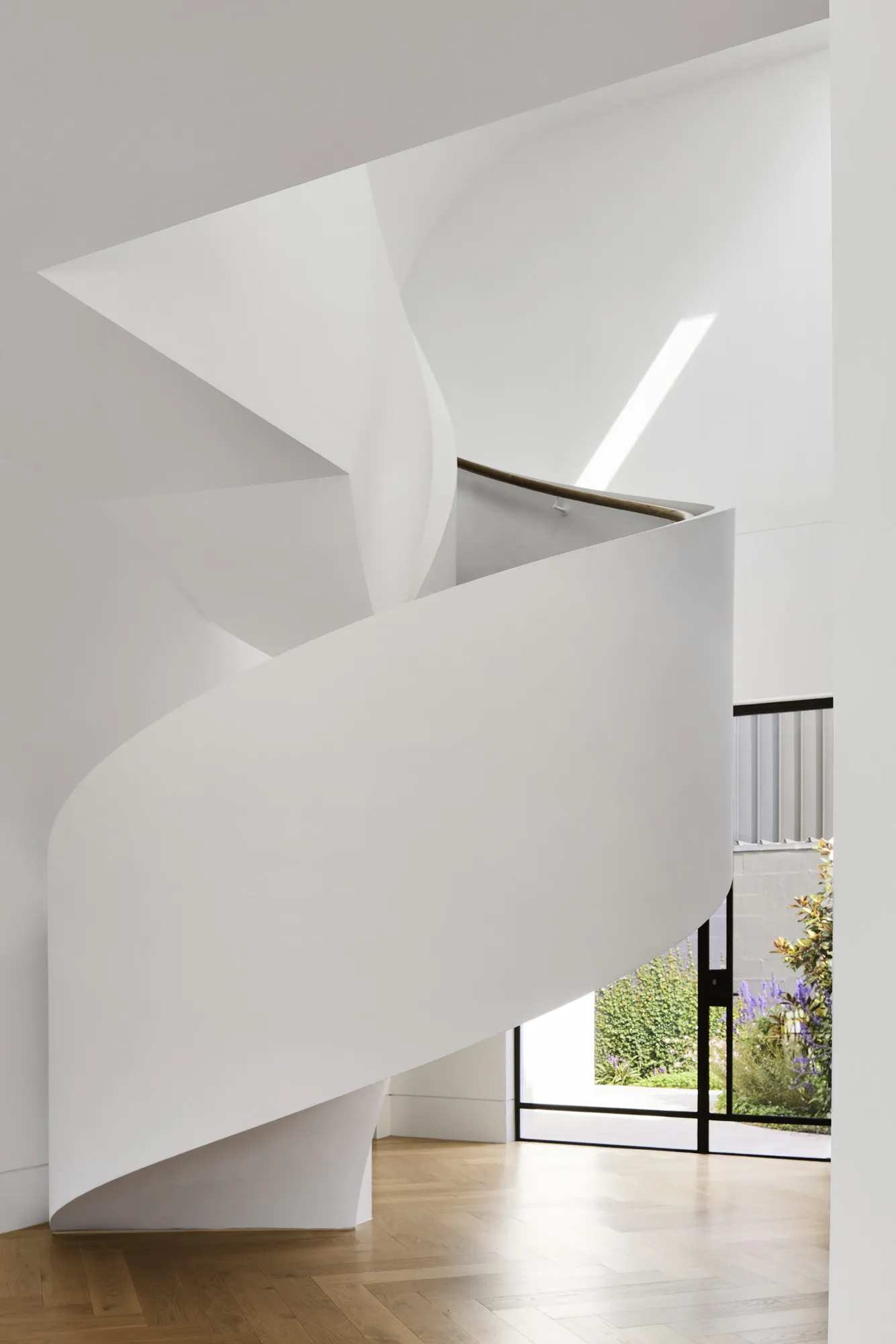 Sculptural all-white curved staircase with timber floors and black-framed garden door beyond