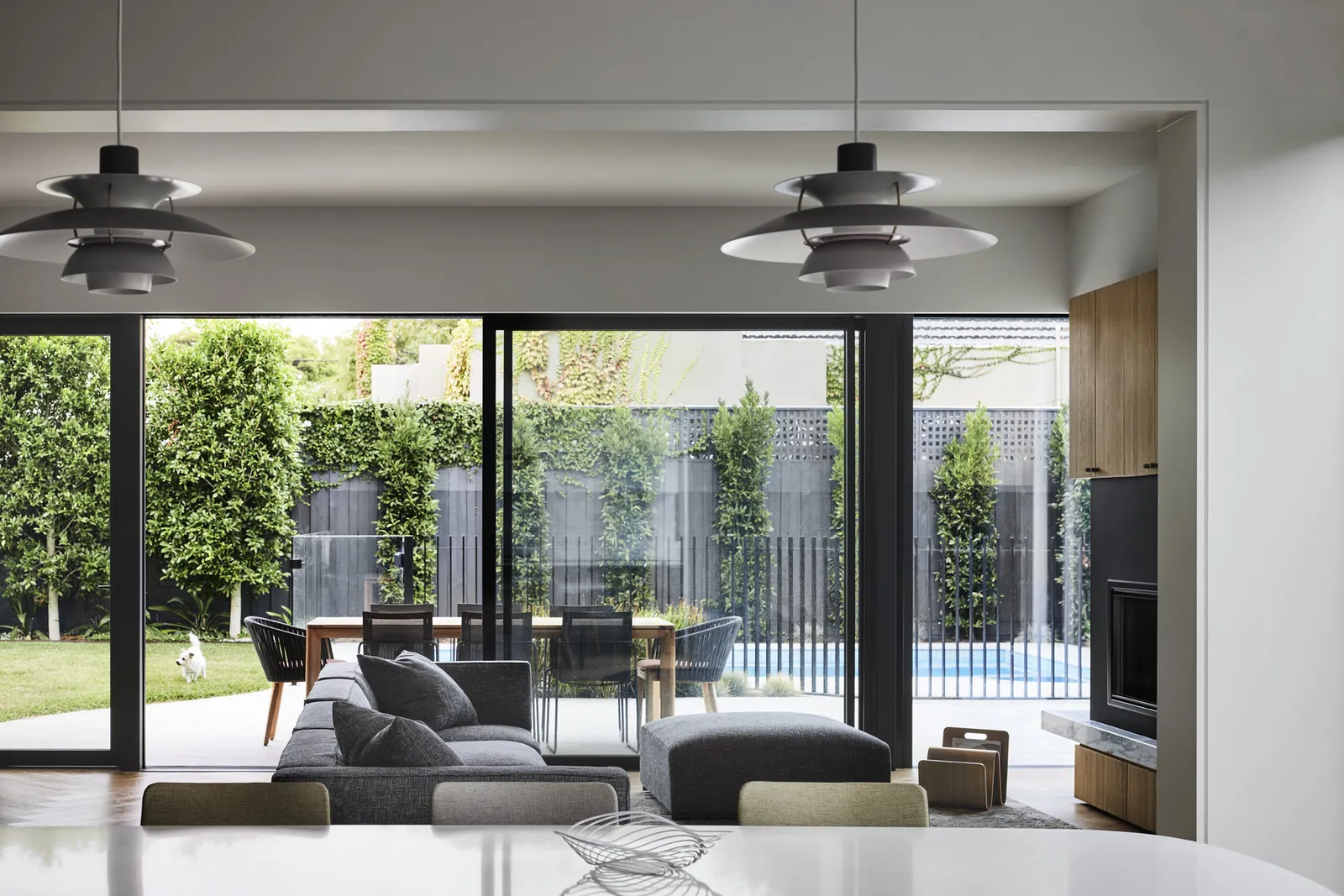 Open-plan living area with grey sofa, pendant lights and large sliding doors opening to pool garden